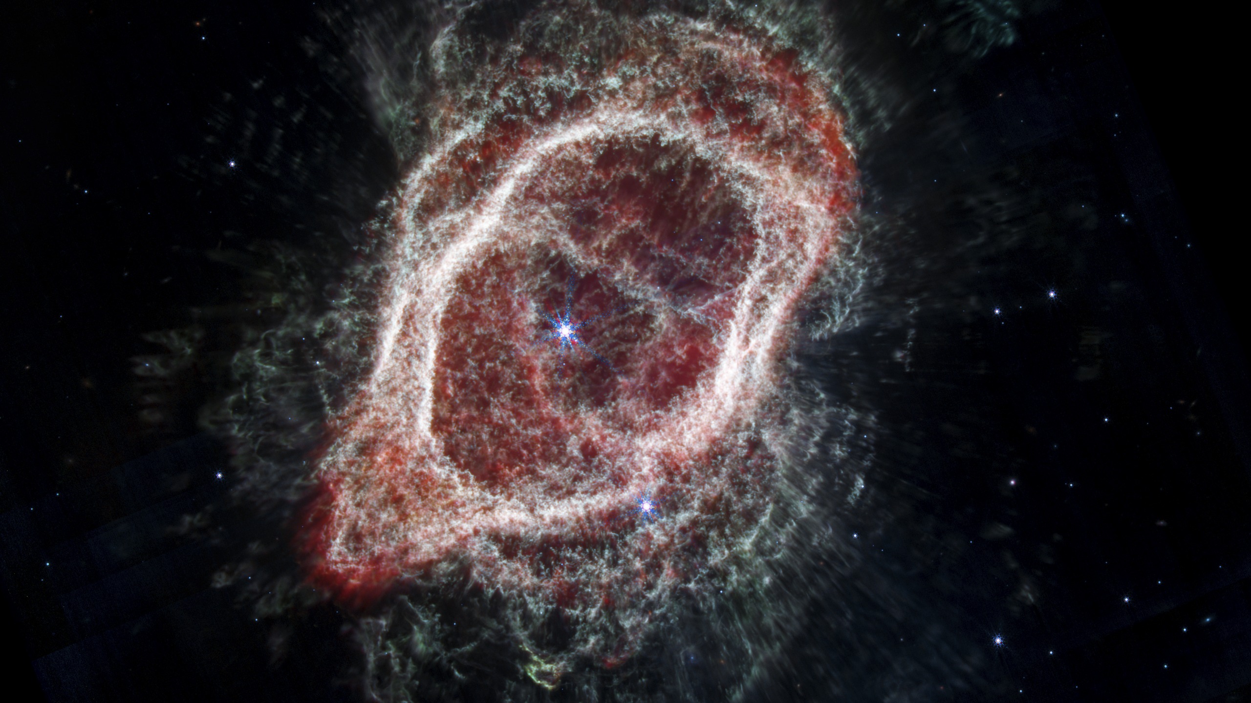 The same Southern Ring Nebula in mid-infrared light, showing a very different color pattern of red and white, tracing the cooler dust and gas instead of the hot gas.